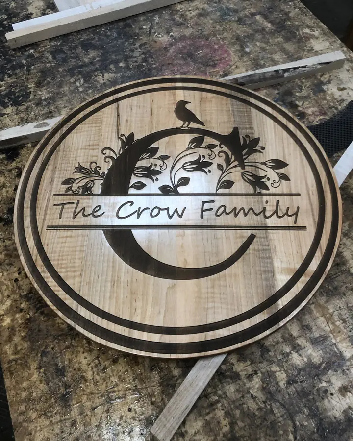 Round maple sign laser engraved with a floral C monogram, a crow and The Crow Family