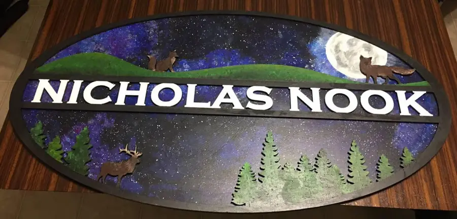 Oval layered wood sign reading Nicholas Nook, hand painted with a night sky, moon, foxes, elk and pines
