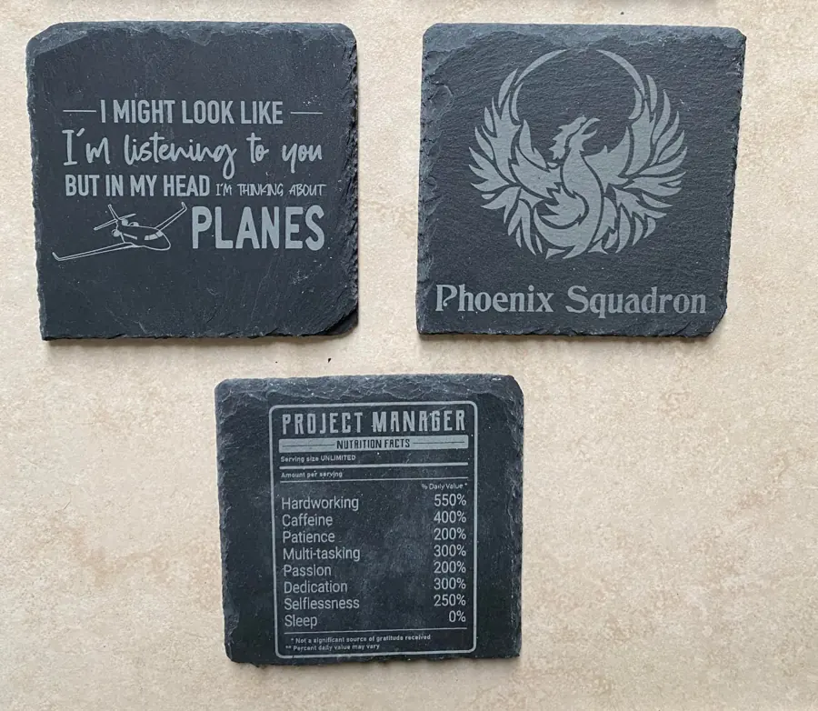Three engraved slate coasters for an aviation team: a planes quote, a Phoenix Squadron crest and a project manager nutrition label